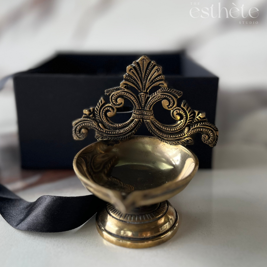 Decorative brass oil lamp with intricate design on a white surface, branded 'esthte'.